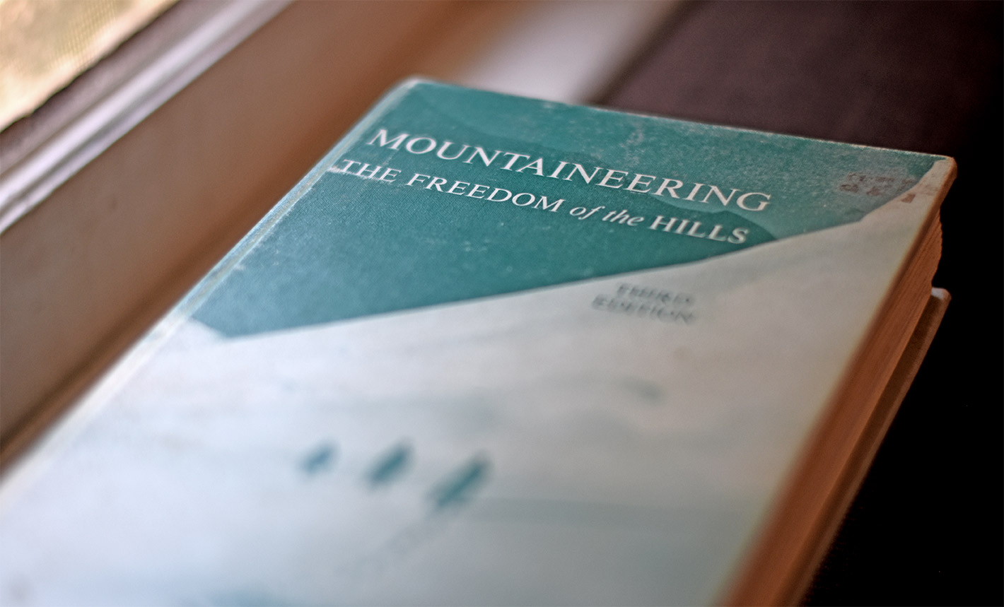 Mountaineering Freedom of the Hills book, with aqua and cream colored cover with mountaineers ascending a snow-covered peak