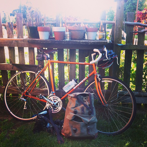Orange Bianchi bike leaning against a fence with pots on it with a salt and pepper Swiss rucksack in the foreground