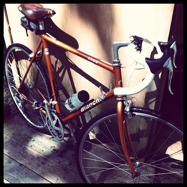 Orange Bianchi bike with white handlebar tape, brown leather Brooks saddle, and water bottle