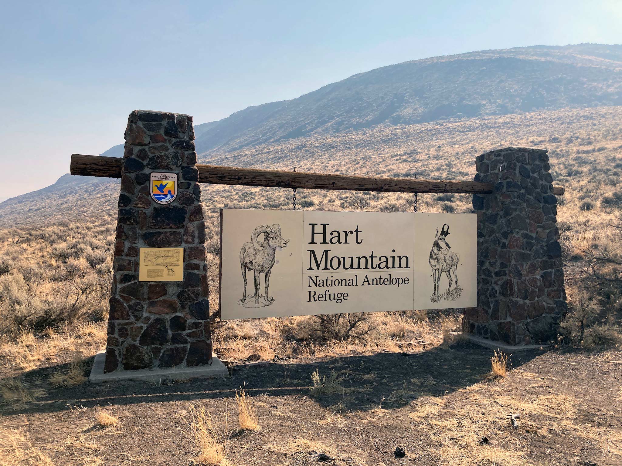 Stone pillars hold a large sign that reads Hart Mountain National Antelope Refuge with a mountain rising in the background