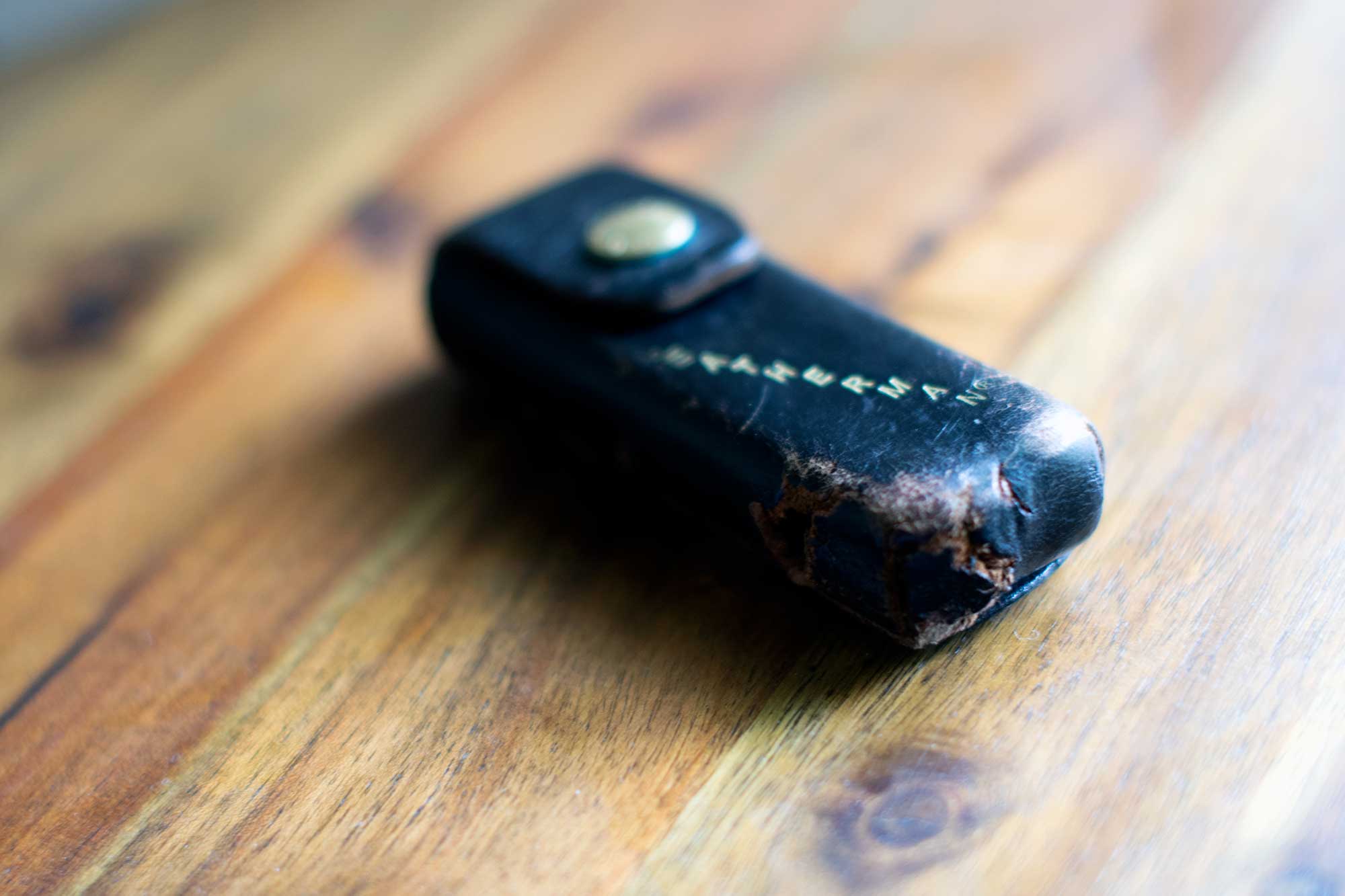 Black leather sheath with the gold embossed Leatherman on it with a noticeable tear in the bottom