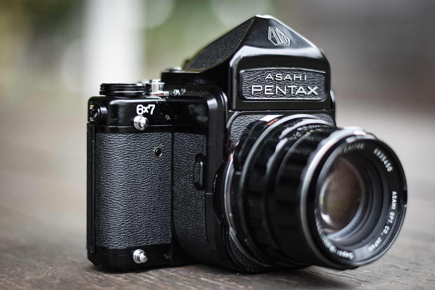 Large black camera with a lens attached, Asahi Pentax embossed on the front, 6 x 7 inscribed on right side, and knobs and silver accessory mounts