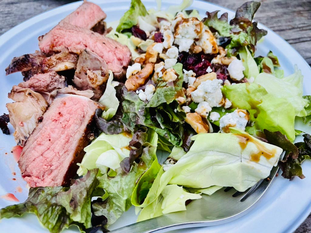 Rare steak sits alongside a colorful salad with nuts, blue cheese crumbles, cranberries, and a bed of lettuce