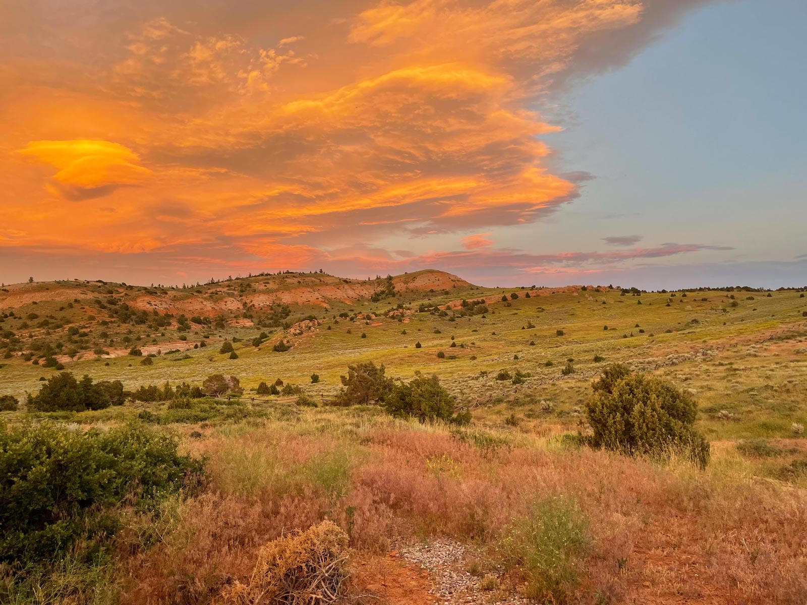 Sunset light illuminates in orange clouds over open land with a bluff