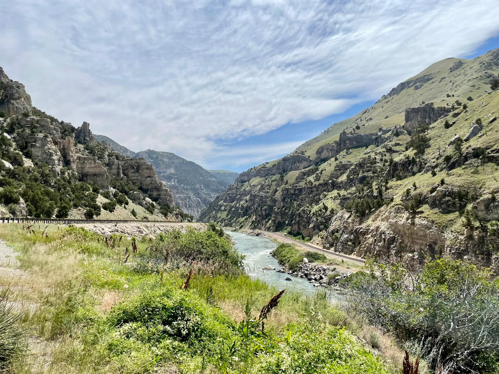 A river winds through high canyon cliffs with a road and guardrail on one side