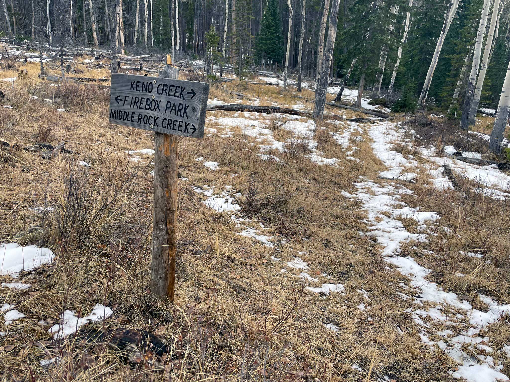 A weathered sign reads Keno Creek pointing to the right, Firebox Park pointing to the left, and middle rock creek pointing to the right with snowy trails leading between trees