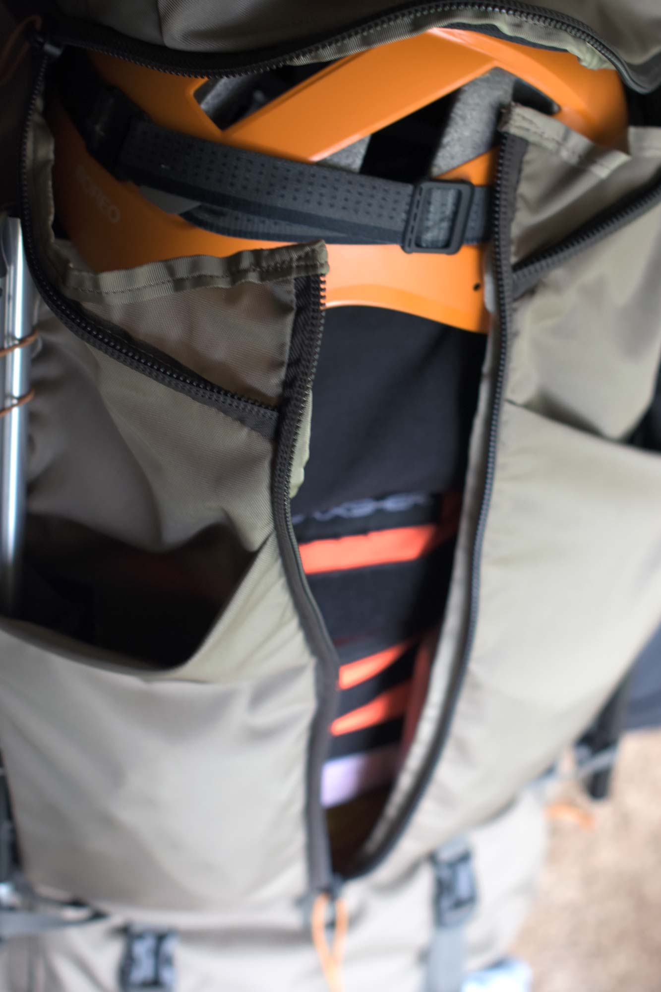 A tan bag with three zippers unzipped to reveal the interior of the bag which shows an orange helmet and black and orange modular bags inside