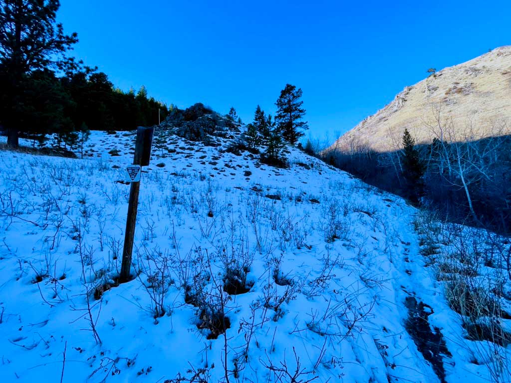 Snow covers the ground in the shadow of the mountain while sun shines on a snowless hillside in the background