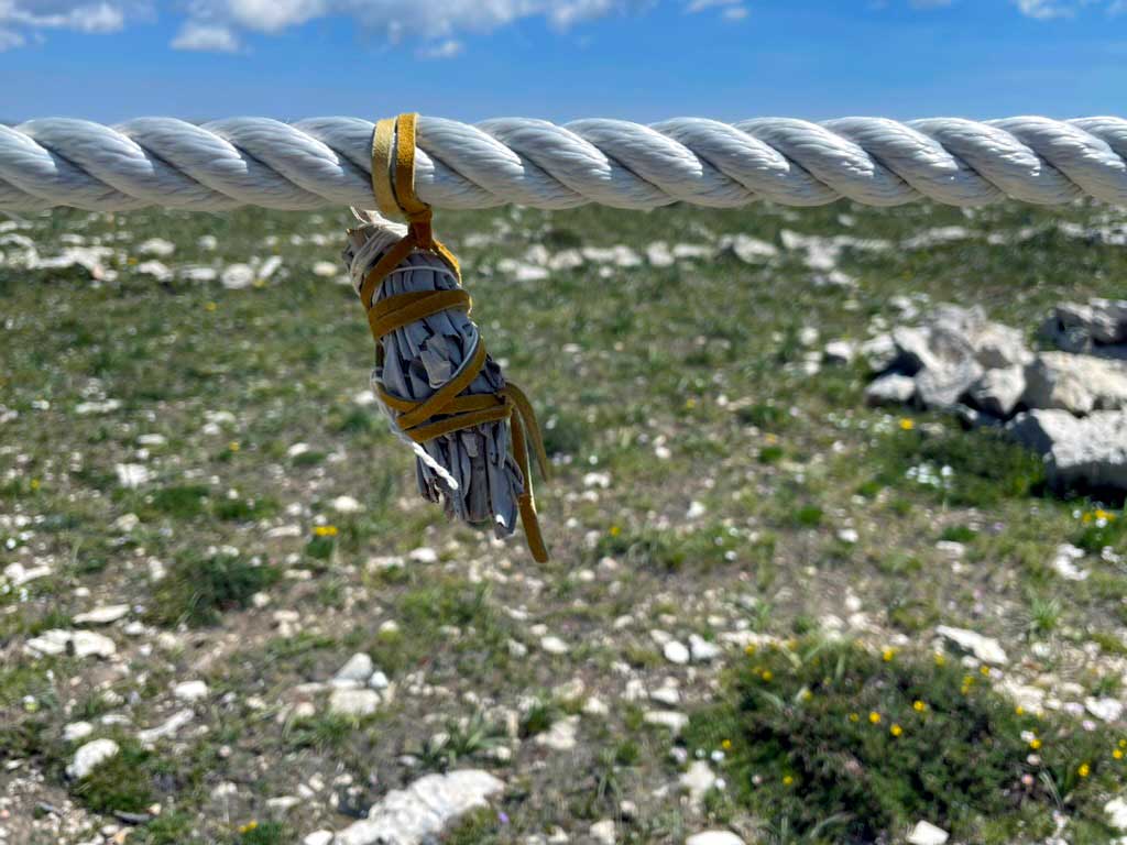 A white rope with a bundle of sage wrapped in leather with grass and rock blurred in the background