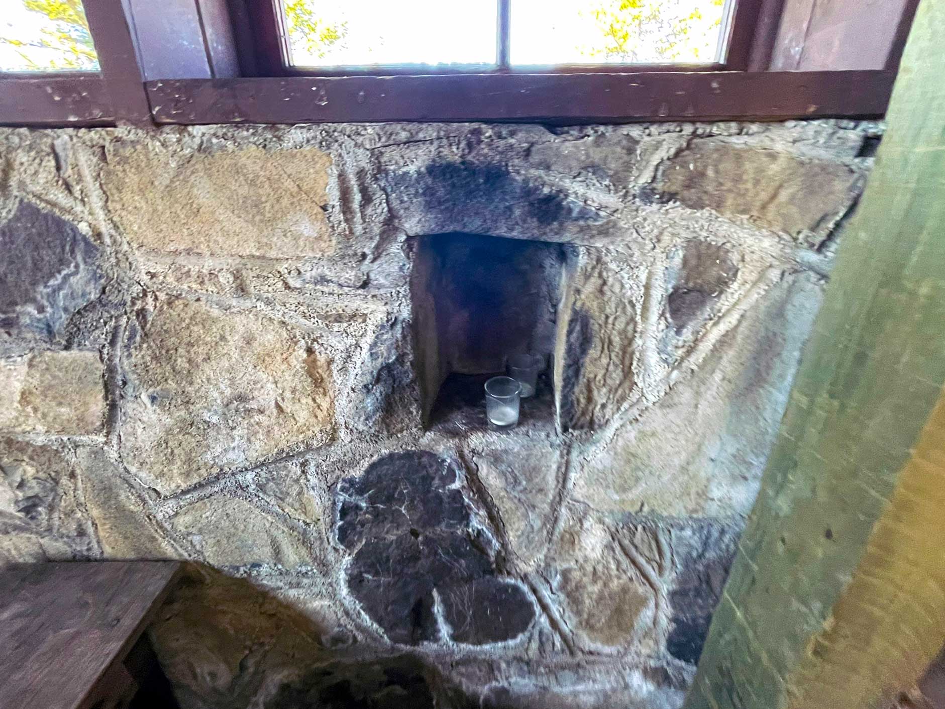 A stone wall with a rectangular shelf built in with black burn marks on the stone and a candle sitting in the shelf