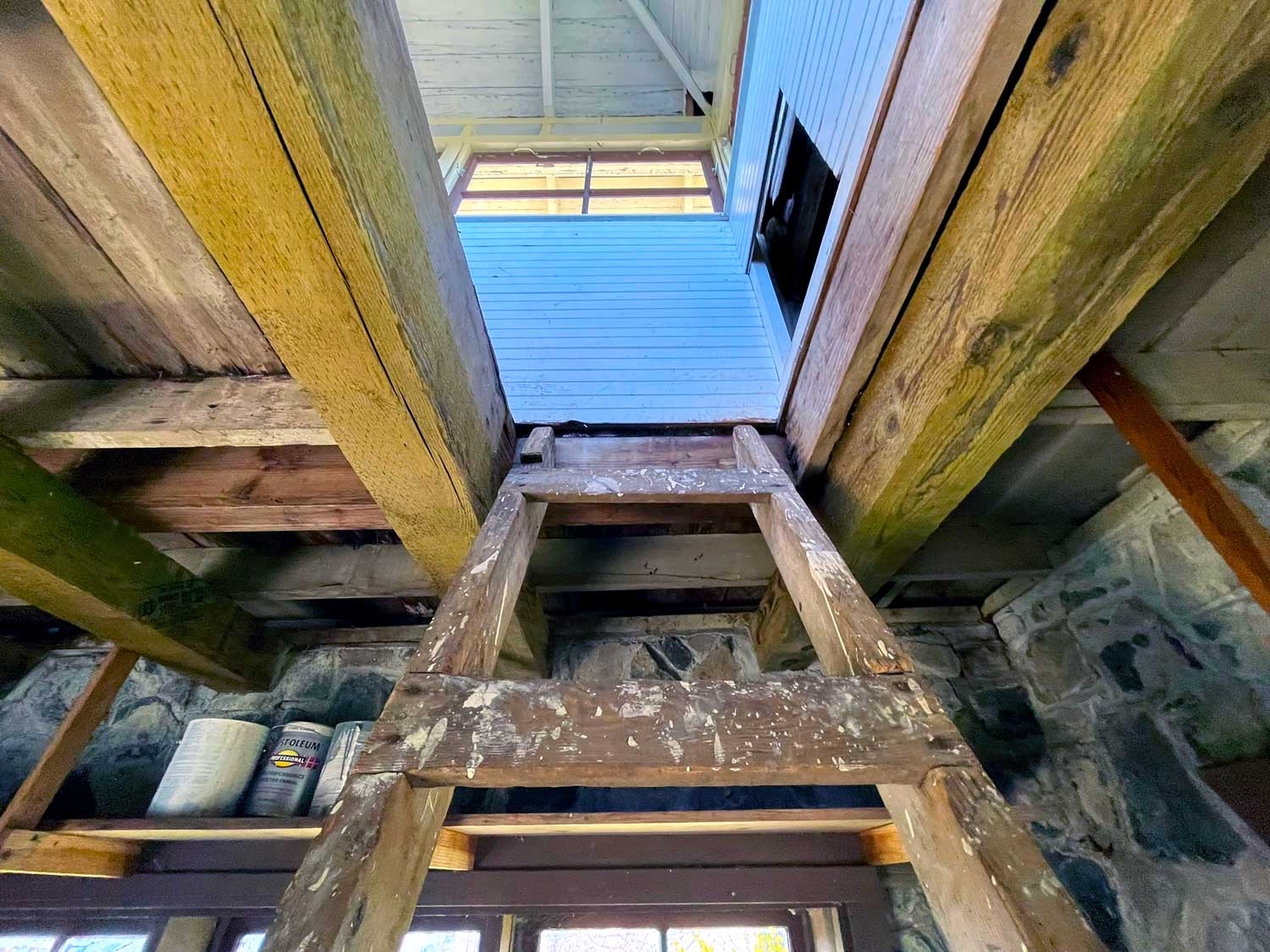 A wooden ladder leads to the upper part of a stone building; the ladder is stained with drops of white paint