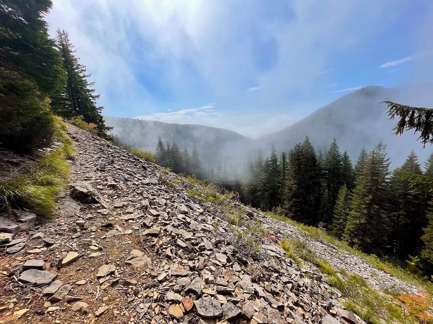 A rocky trail with a drop off with forested hills in the background