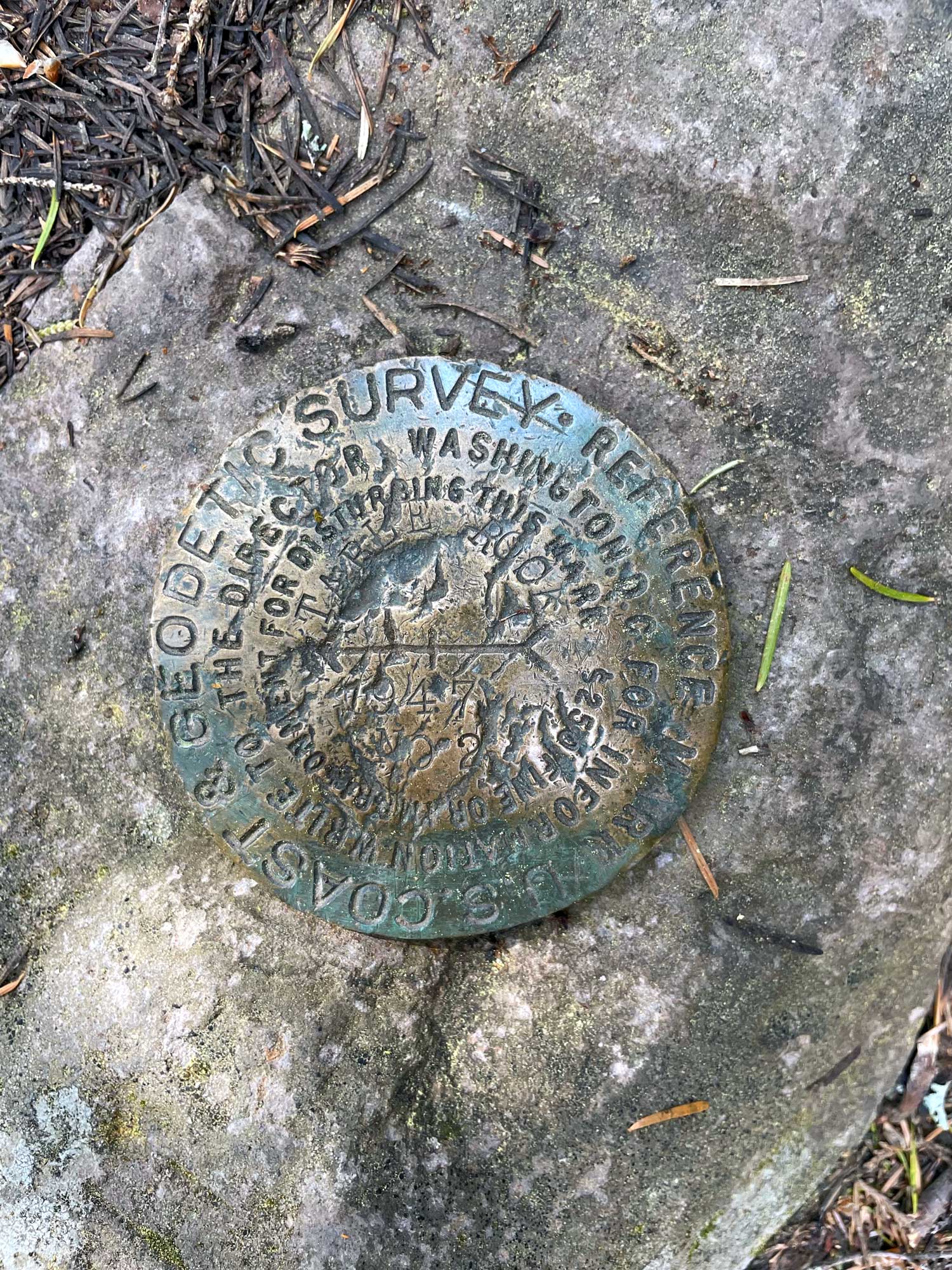 A metal survey marker that reads US Coast and Geodetic Survey, for information write to the director Washington DC, $250 fine or imprisonment for disturbing this mark, 1947 No. 2