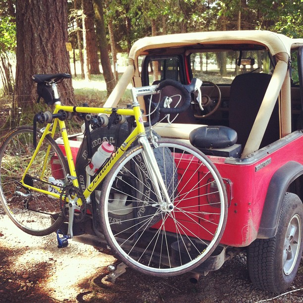 A red jeep with the top down and a yellow bicycle on a rack on the back of the vehicle