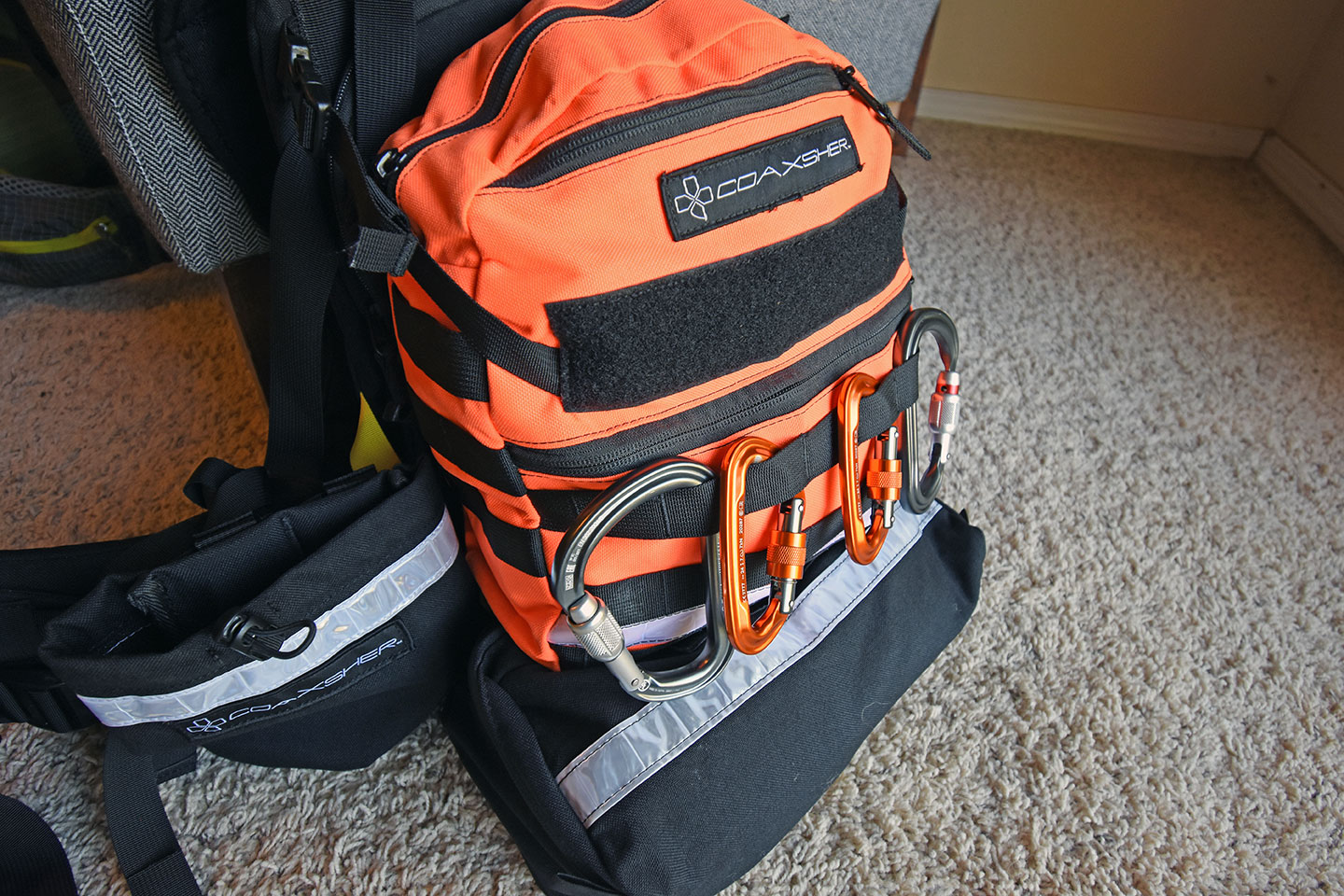 Coaxsher brand orange and black pack modules on a harness with carabiners attached
