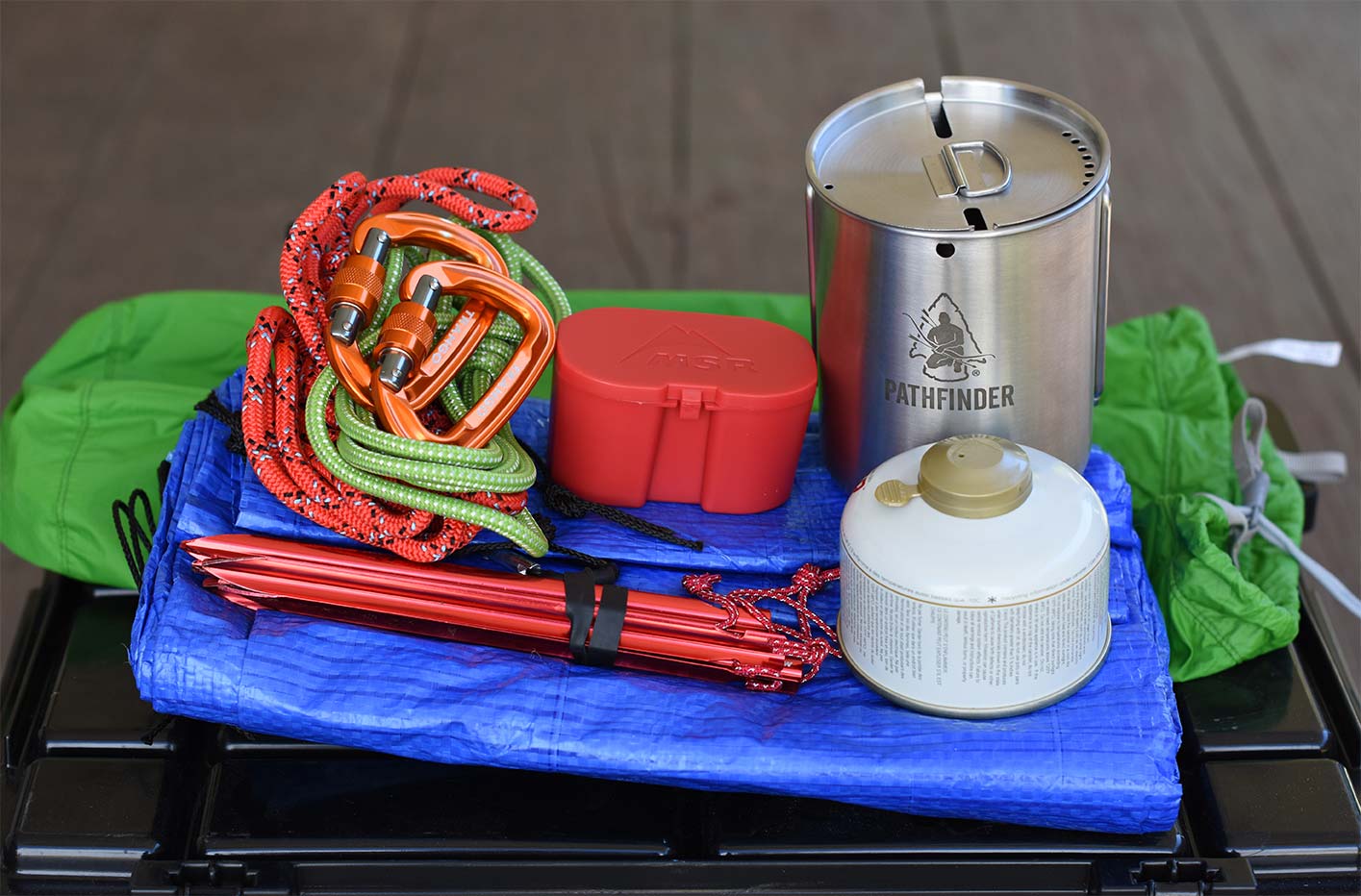 Tarp, stove, cup, rope, stakes in front of a green bag
