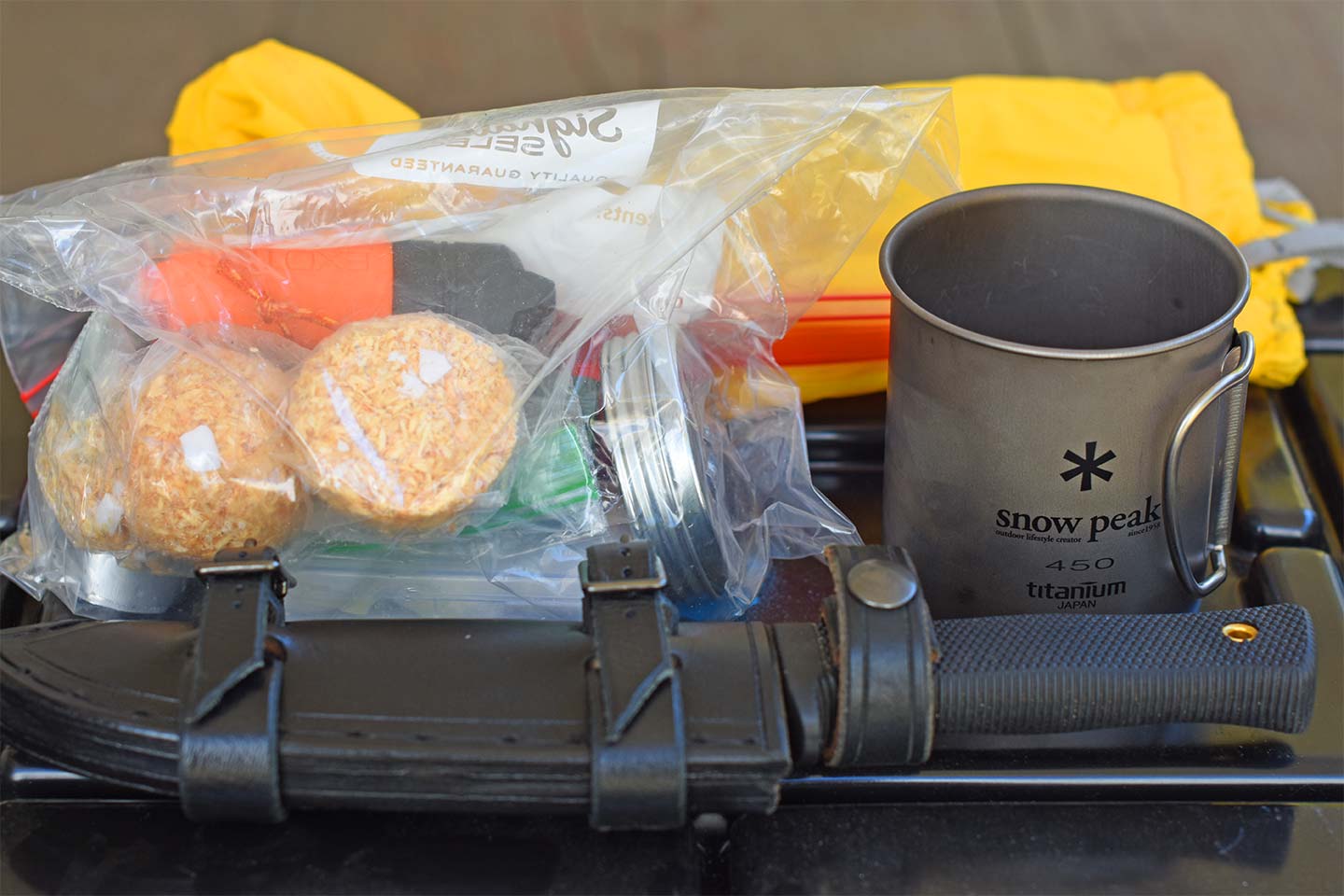 Fixed-blade knife, ziplock bag with fire starters and matches, with a yellow bag in the background