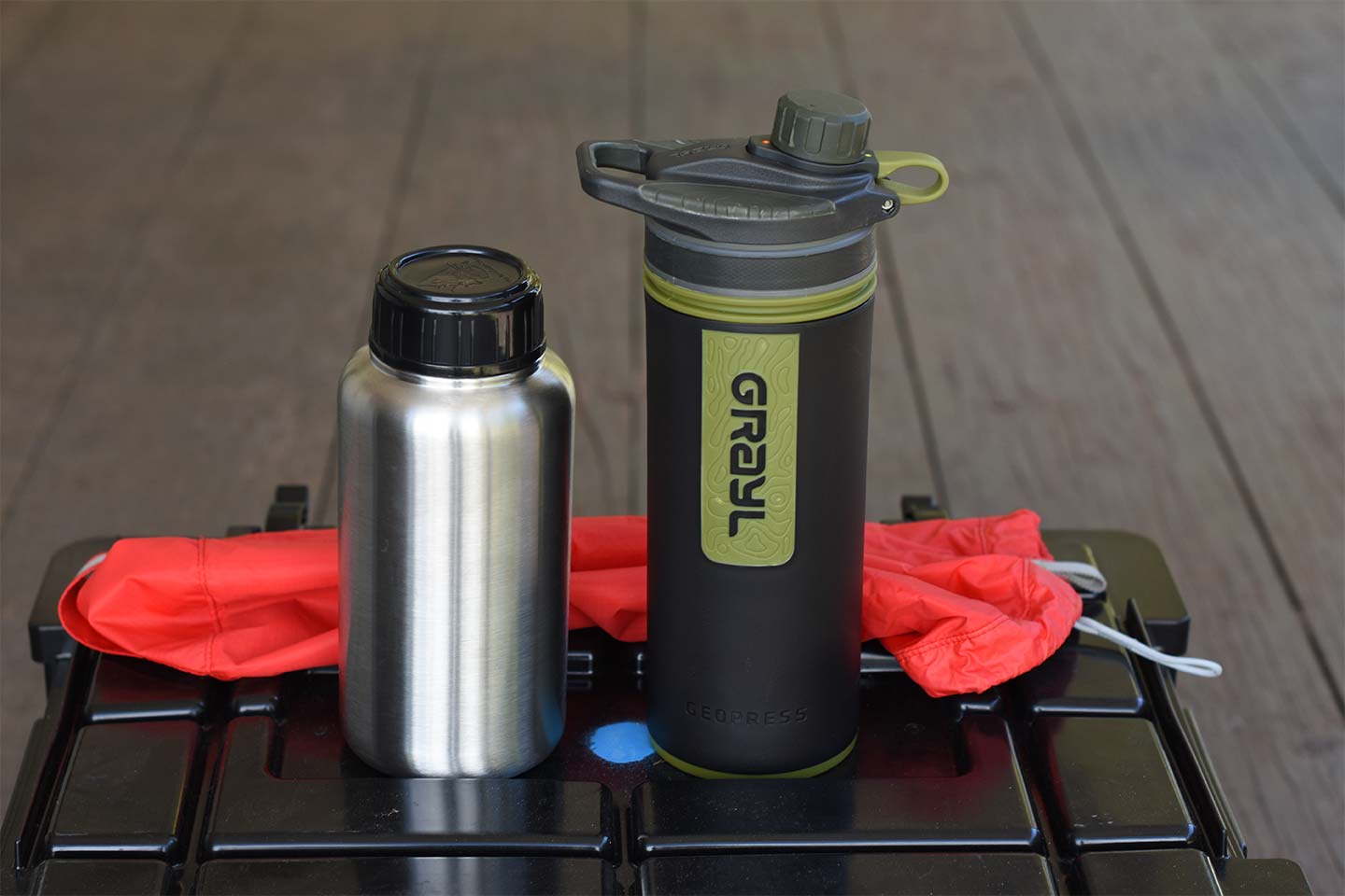 Metal water bottle and Grayl geopress bottle in black and green, with a red bag in the background