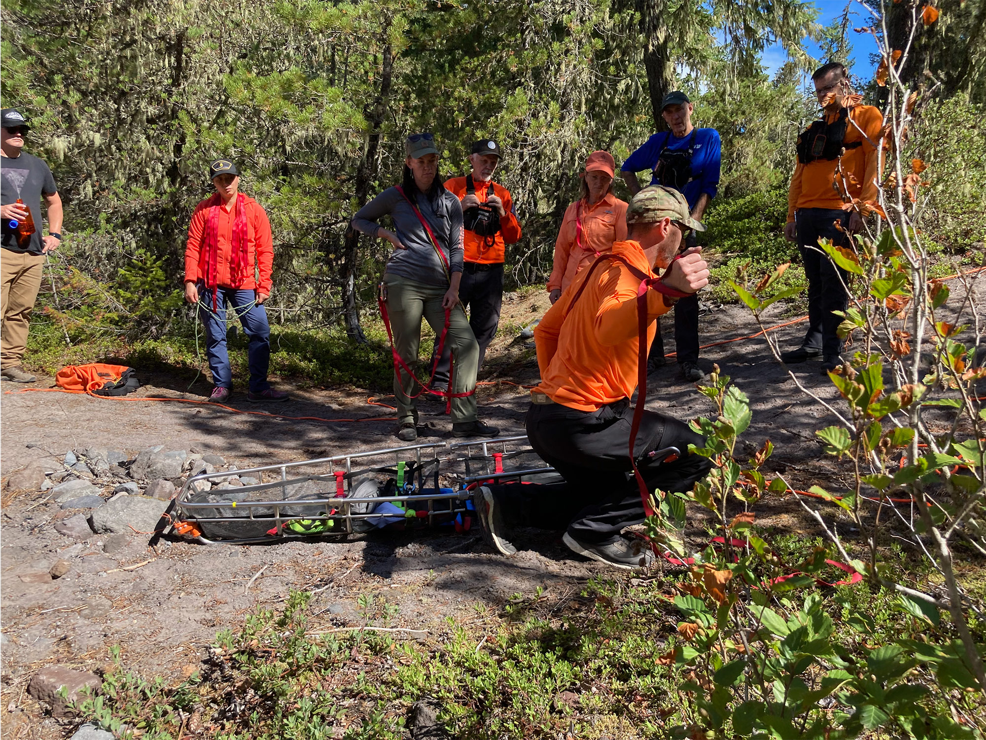 Several search and rescue members in the field watching a demonstration on litter packaging